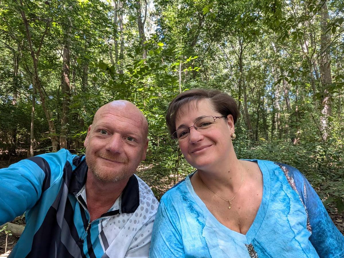 Stan and his wife on a wooded trail, smiling at the camera.