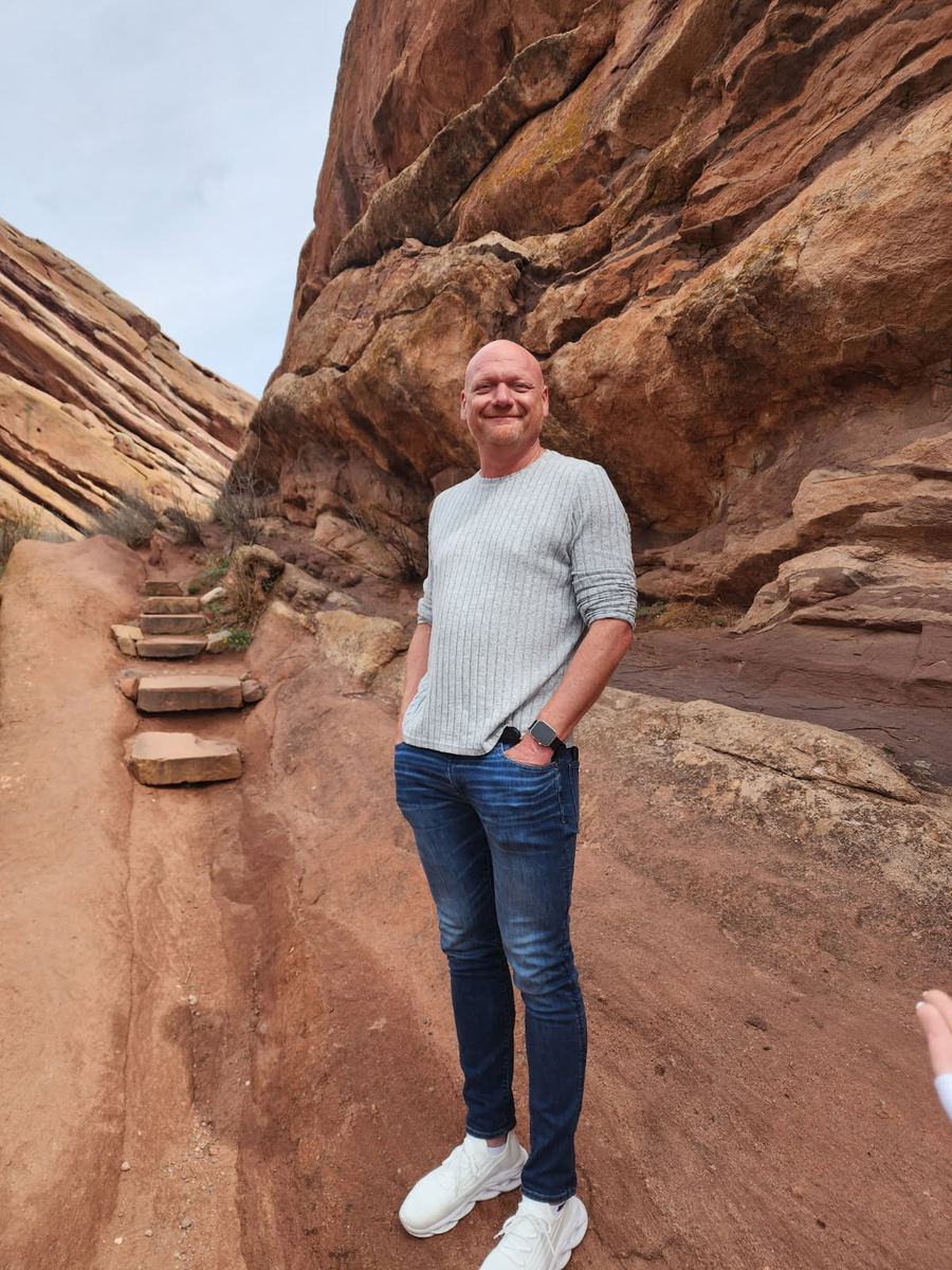 Stan standing on a red rock trail, smiling, hands in his pockets.