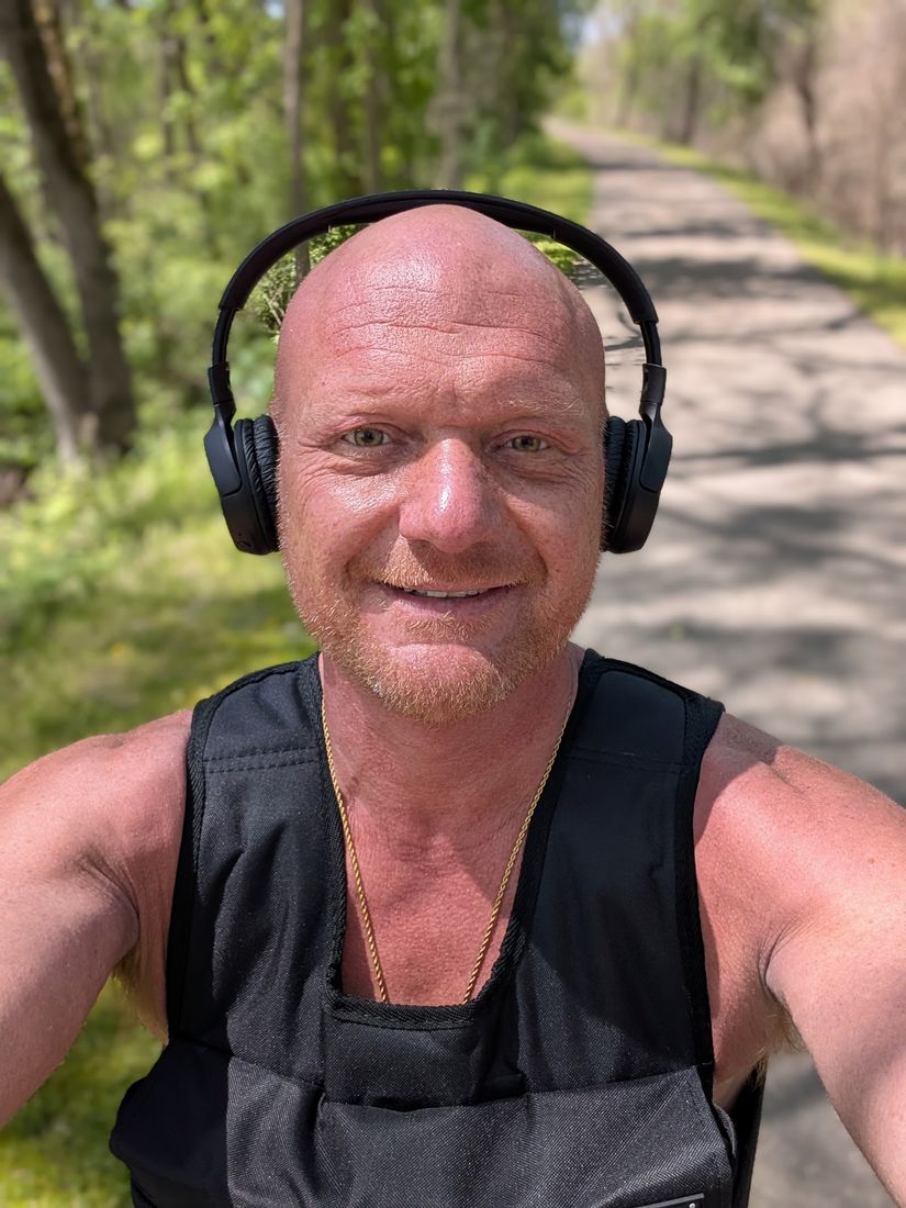 Stan on a wooded path wearing headphones and a black training vest.